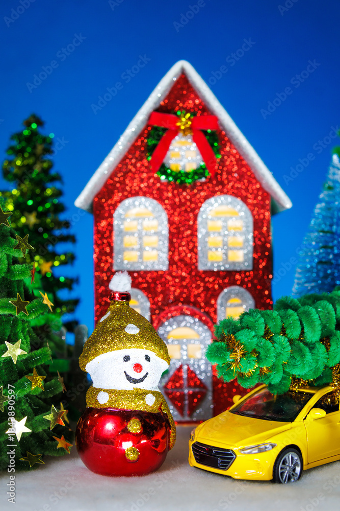 Fototapeta premium A snowman and a yellow car near a red Christmas house