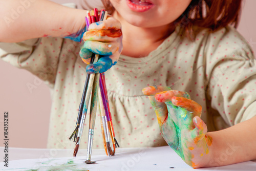 A child holding paintbrushes with colorful hands — a symbol of early creative freedom.