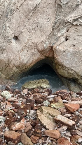 Coastal rock formation with a natural blowhole spraying seawater, waves crashing over rugged stones, capturing dynamic marine motion near the beach.