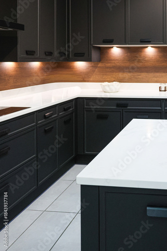 Modern kitchen interior with dark cabinets, white countertops, wood backsplash, and under cabinet lighting creating contrast