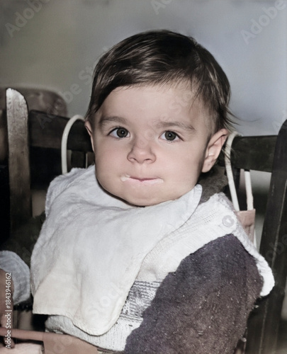 Vintage portrait of a one year old girl eating. The child's mouth is in porridge. Retro photo from 1995.