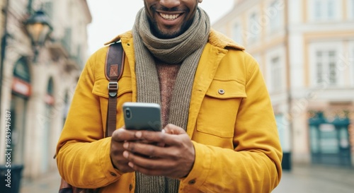 Man using smartphone while walking on city street with warm jacket and scarf