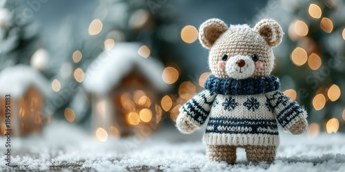 Crocheted bear in blue fair isle sweater stands in snowy village with glowing Christmas lights..Perfect for holiday ads, handmade toy features, or cozy winter campaign banners.
