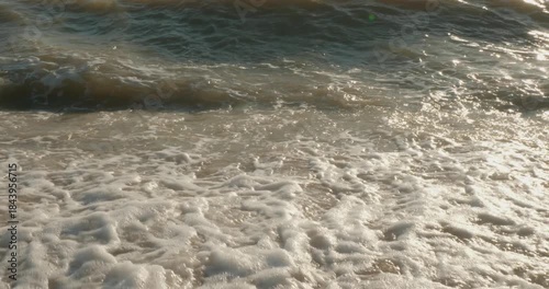 Beautiful sea waves run to the golden shore Small ocean waves with white foam gently break on the sandy shore while sunlight reflects on a calm surface of the water creating a peaceful sea landscape.