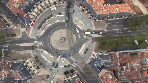Top down drone shot of dynamic busy roundabout with tram lines and cars in Bordeaux France forming geometric pattern