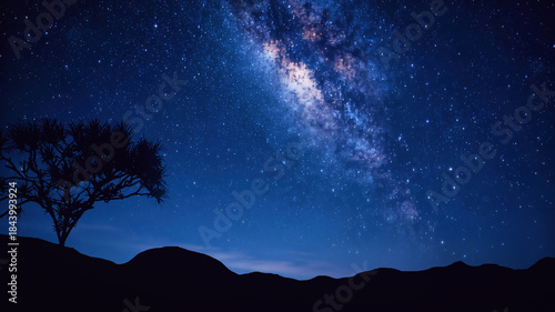 Starry night sky with silhouette of a tree over rolling hills under Milky Way