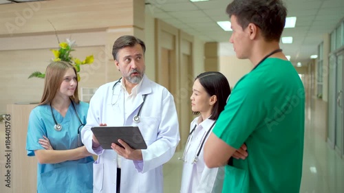 Medical team discussing patient data on tablet in hospital hallway.