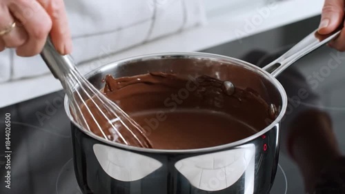 Whisking melted chocolate in saucepan on stovetop for sweet dessert sauce preparation