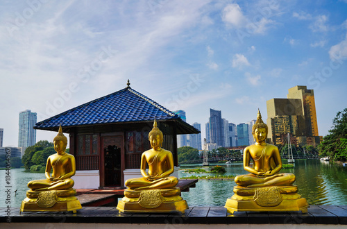 Serene Gilded Buddhas statues in meditation in contrast with the modern city skyline of Colombo at the picturesque Seema Malaka temple,Beira Lake,by architect Geoffrey Bawa,1976 in Colombo,Sri Lanka