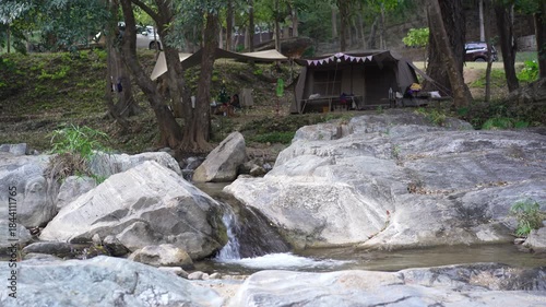 nature camping tent on natural water stream by waterfall flow and rocks to camper family relax in tree garden forest at phalad waterfall in lan sang national park campsite on holiday with stream sound