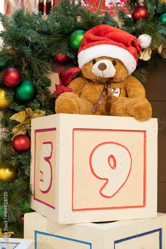 Cute Teddy Bear with Santa hat on Christmas blocks beside festive tree decoration