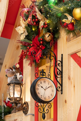 A charming vintage clock mounted on a wooden wall, featuring a rooster weather vane and a hanging bell. Surrounded by festive Christmas decorations and rustic decor creating a cozy holiday.