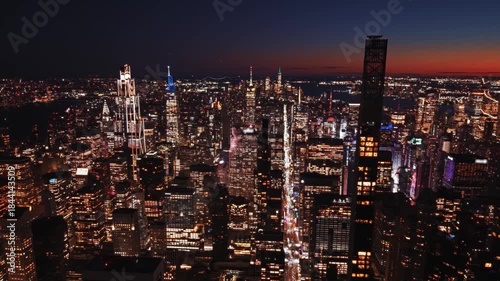 Elevated view of the Midtown Manhattan skyline at night featuring illuminated skyscrapers and city lights. Dense urban cityscape with modern architecture and dark sky