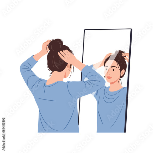A woman adjusts her hair while looking at her reflection in a large mirror
