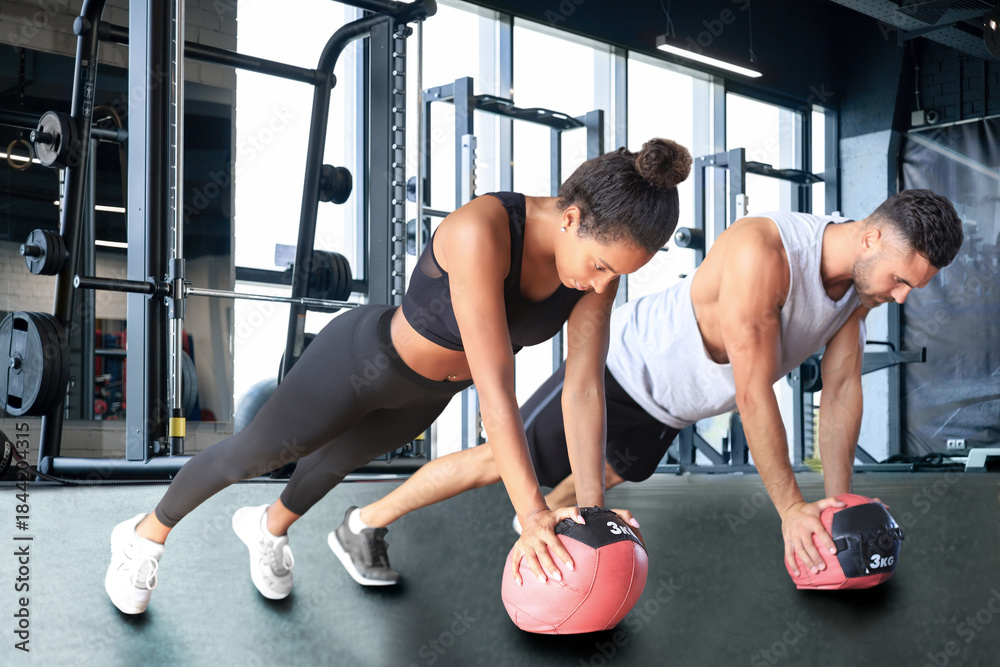 Naklejka premium Beautiful young sports couple is working out with medicine ball in gym.