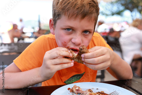 Young caucasian boy enthusiastically eating fried chicken leg with messy face