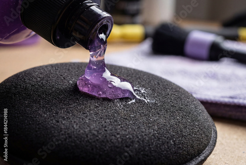 Auto detailing supplies. Pouring purple polishing compound onto a black foam buffing pad. Preparation for car paint correction