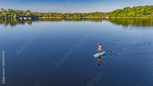 Active woman paddling SUP board on beautiful Lough Key lake, green islands and forest summer landscape on background, stand up paddling water adventure outdoors, Ireland