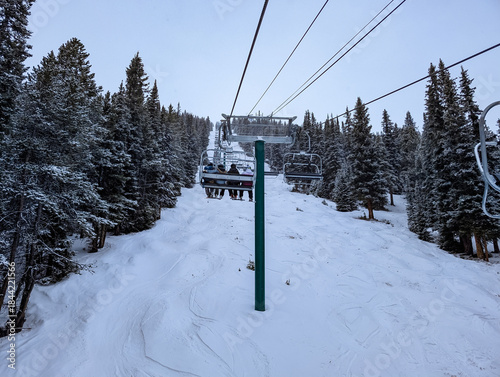 Skiers and snowboarders on a chairlift in high mountains against a clear blue sky with plenty of copy space. Skiing on a chairlift in a winter landscape on ski hills in Canada.