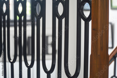 Close-up of a black wrought iron railing with a wooden handrail, showcasing intricate decorative metalwork