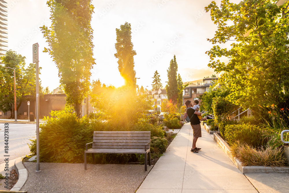 Fototapeta premium Father holding his baby while walking in a vancouver city park at sunset