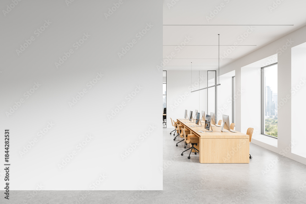 Obraz premium Modern office interior with large white empty wall for poster mockup and shared workstation area with wooden desks and computers near big windows. 3D Rendering