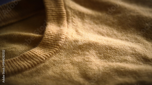 Warm-toned close-up of soft yellow woolen sweater with fuzzy texture and ribbed collar. Pullover made of natural fabric