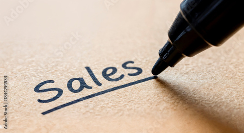 close-up of a marker pen writing the word “sales” on a piece of cardboard, selective focus