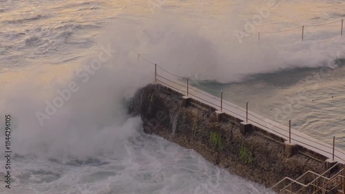 waves crashing over ocean swimming pool in early morning dawn light