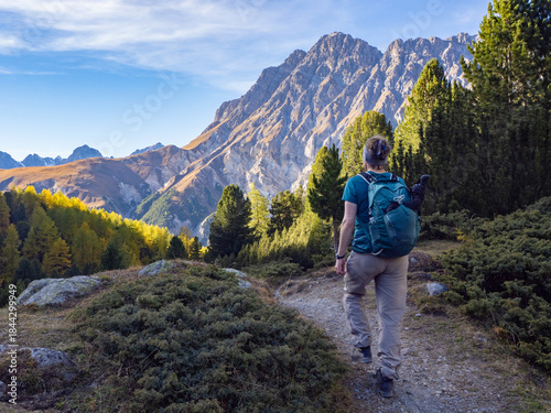 Scuol, Switzerland - October 10th 2025: A female hiker exploring a trail through mountainous forests and alpine peaks.