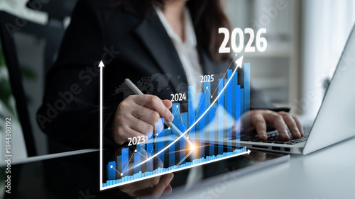 A business professional focuses on a growth graph highlighting years 2023 to 2026. The scene showcases financial planning and performance tracking on a laptop. Tessel