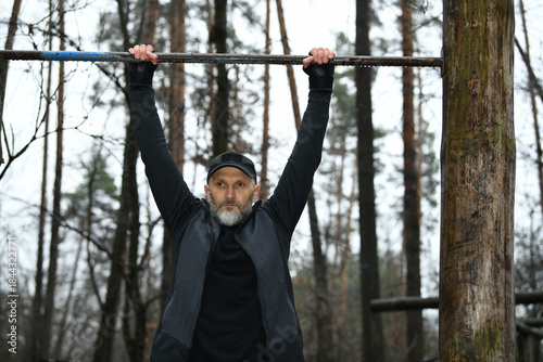 Man training outdoors with pull-up bar in forest during a cloudy day