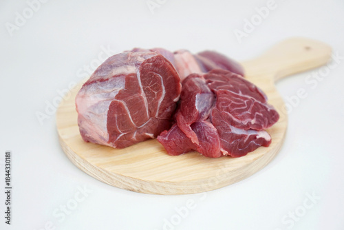 three pieces of raw beef shank on a round wooden cutting board, isolated on white background