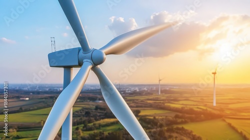 Close up of a large wind turbine with three blades against a dramatic sunset sky over a rural landscape