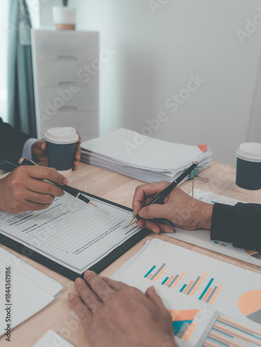 A male lawyer is working in his office, signing a contract with a male client who is seated in his office at a desk with a gavel and scales. (Close-up shot)