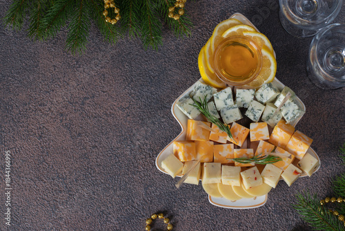 Assortment of sliced cheeses and lemon in Christmas tree-shaped plate on brown table,Top view