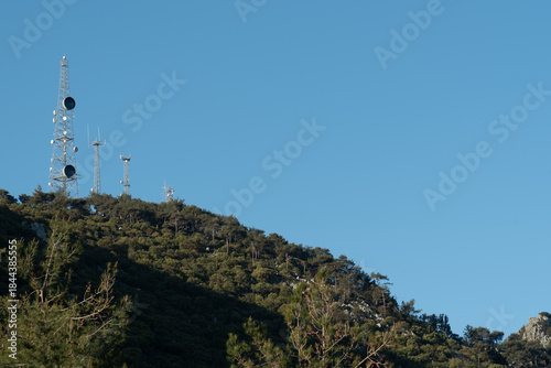 Communication towers stand tall on the mountain under a clear blue sky in daylight hours