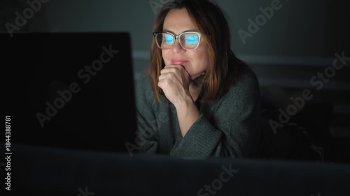 An adult internet addict woman networking concentrated late at night in bed with a laptop
