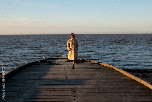 Woman in trench coat walking on wooden pier, enjoying quiet solitude by the sea