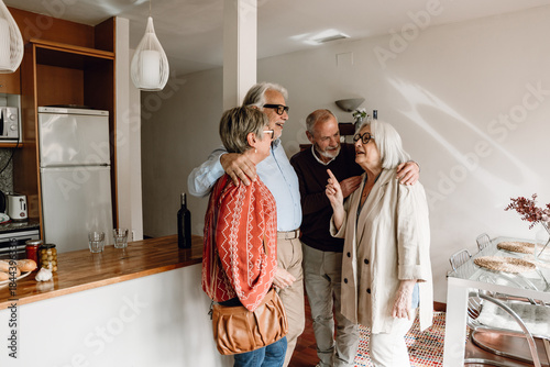 Fotografija A group of four friends stand and smile while hugging and one of them is talking
