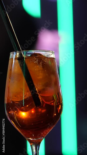 Vertical video footage of a cocktail in the Spotlight. A Crystal Glass with Citrus and Ice Against a Blurred Ballroom Dance Floor. Couples are dancing in the background against. Slow motion 2x