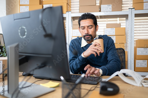 Small business owner working late at warehouse office, drinking coffee
