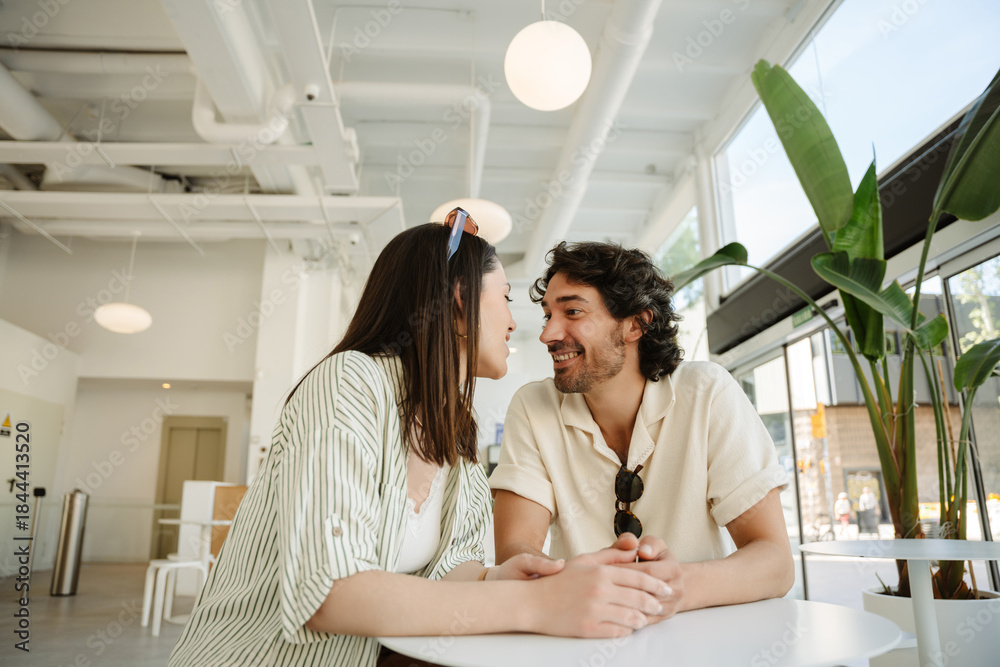 Fototapeta premium Man laughing and listening to woman talking while they hold hands and sit at a table