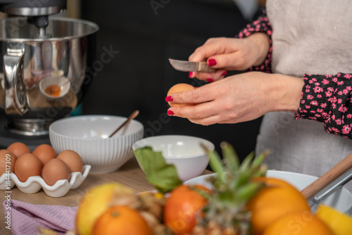 Bilde på lerret Female chef with manicured nails is cracking an egg in a kitchen, surrounded by