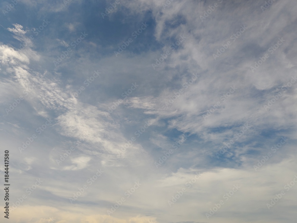 Fototapeta premium Blue sky background with white cirrus and cumulus clouds. Beautiful daytime atmospheric view with soft sunlight. Nature and weather concept.