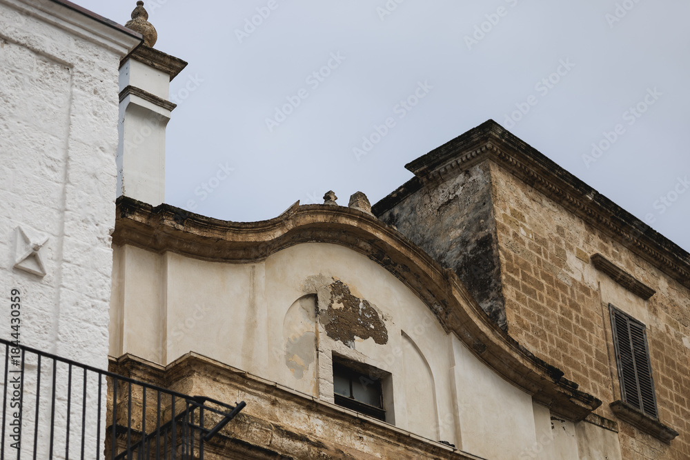 Fototapeta premium baroque facade architecture detail featuring weathered stone, peeling stucco, and curving ornamentation, set against a pale sky, evoking the rustic charm of southern italy.