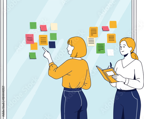 Two businesswomen discuss and organize colorful sticky notes on a glass wall