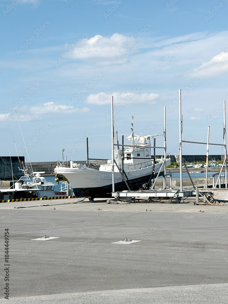 Fototapeta premium Fishing boat undergoing maintenance on a dry dock in a sunny harbor with blue sky and clouds
