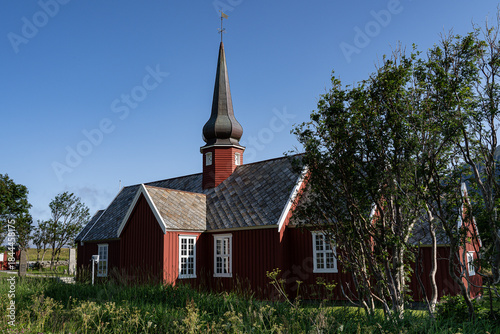 Typical red wooden church in Norway surrounded by green trees during summer season.