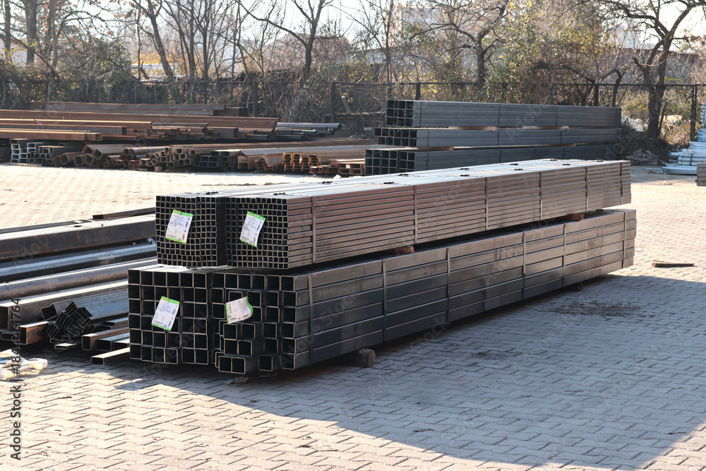Naklejka premium Outdoor view of stacked square and rectangular steel hollow section profiles with labels stored in an industrial metal yard